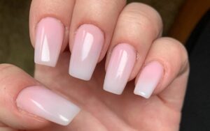 Blizak prikaz ruke sa noktima u suptilnoj roze-beloj ombre nijansi.